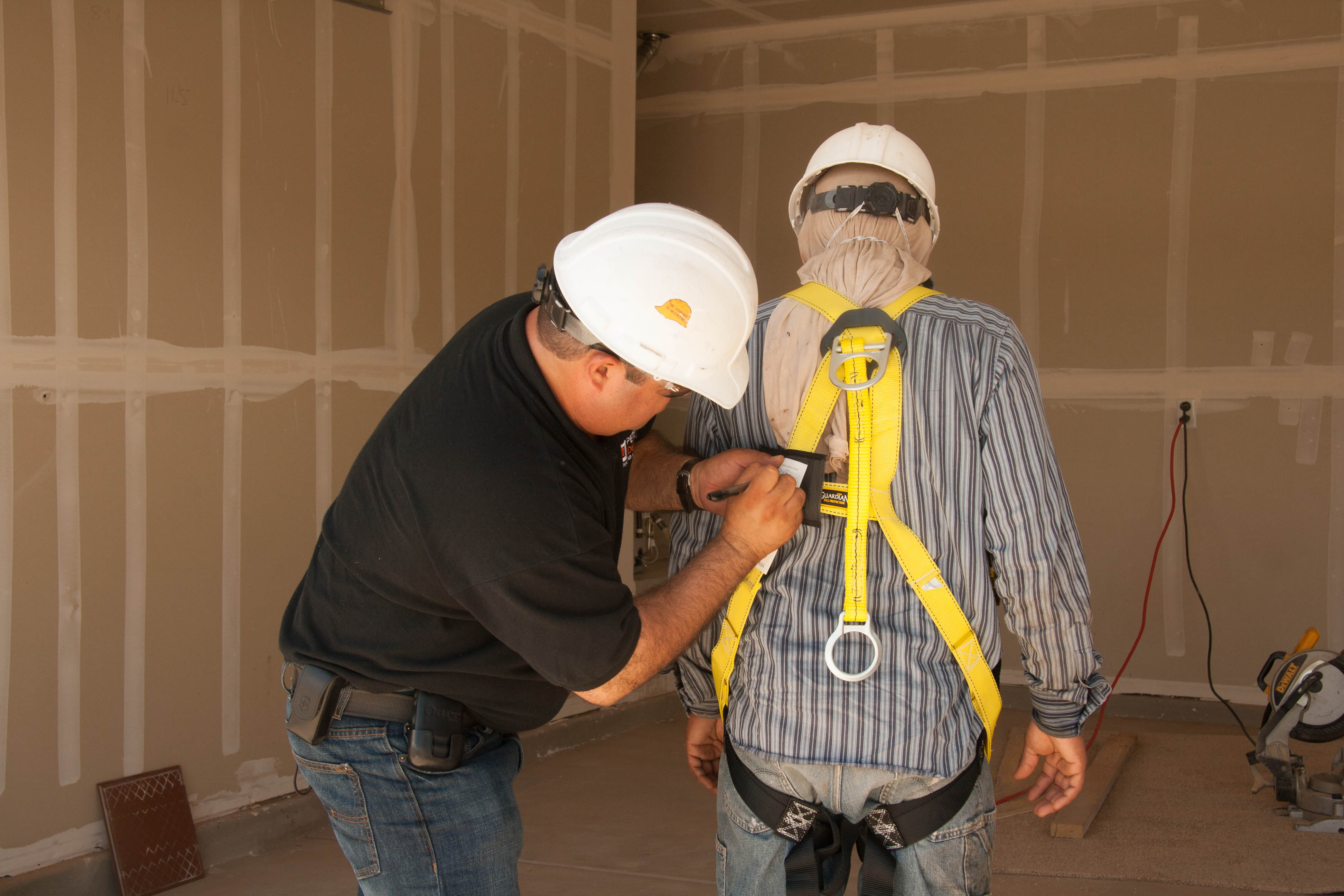 Construction worker helpin another one to set up safety harness